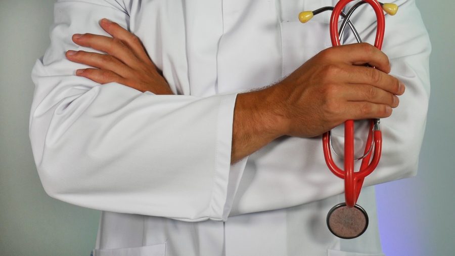 Doctor in a white coat with arms crossed, holding a stethoscope.