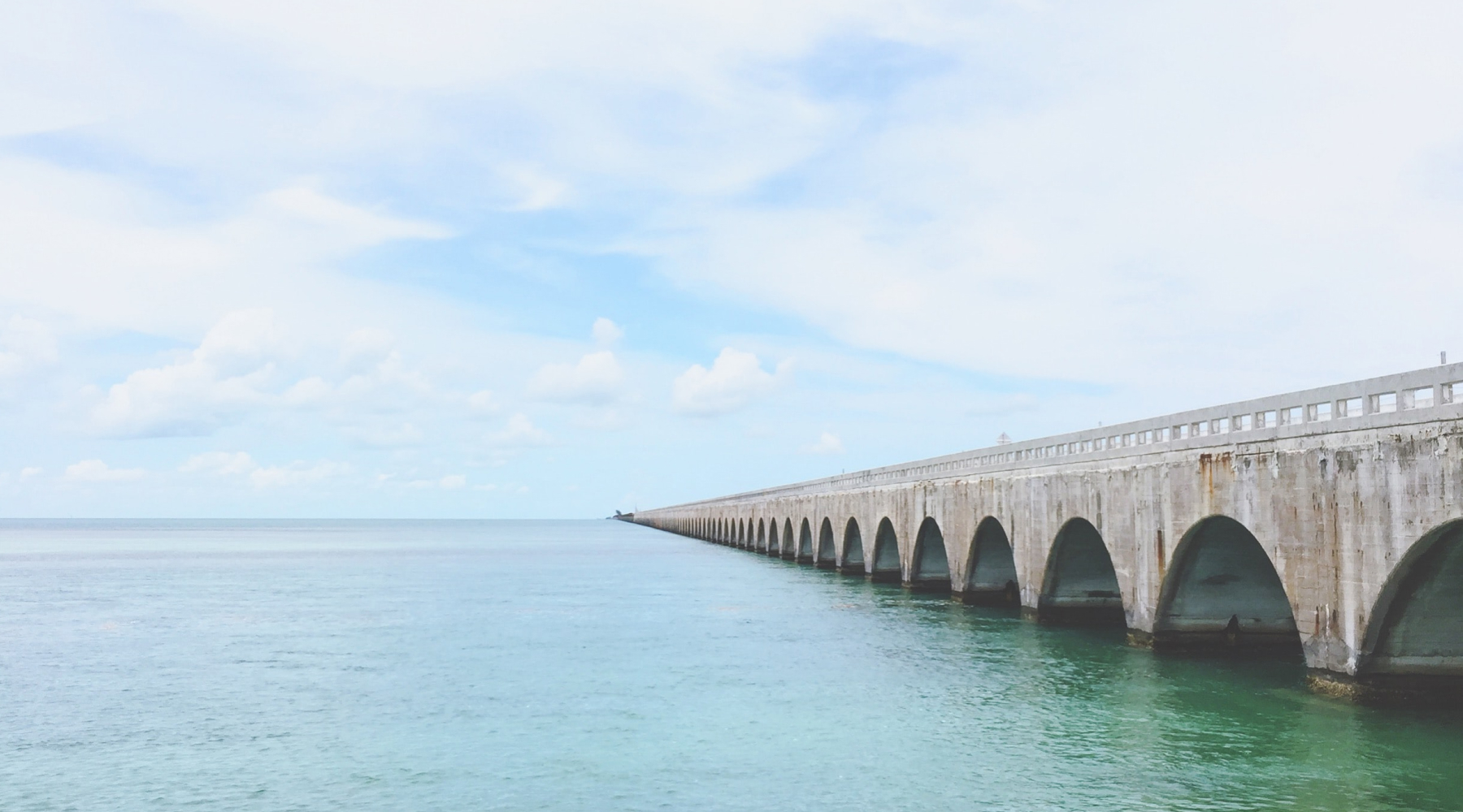 Long concrete bridge extending over calm turquoise water.