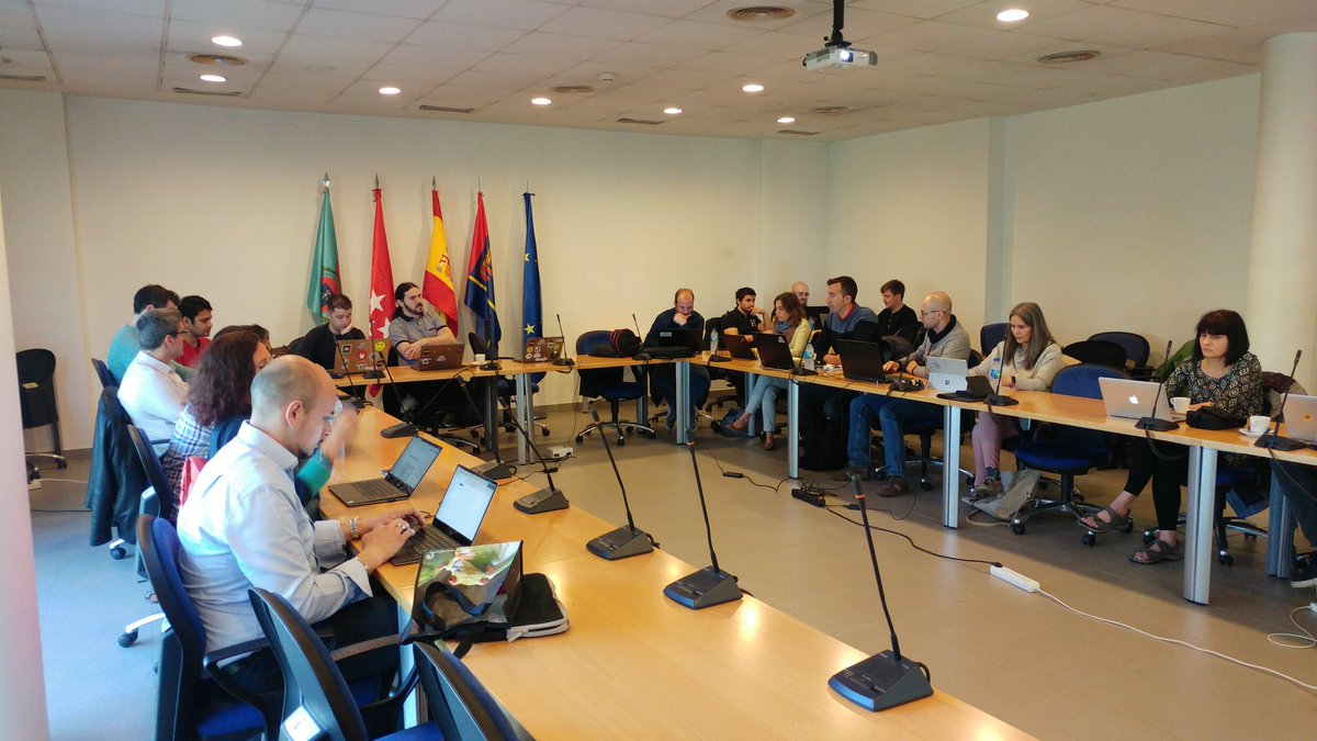 ElasTest project consortium meeting in a conference room in Madrid, with partner flags displayed.