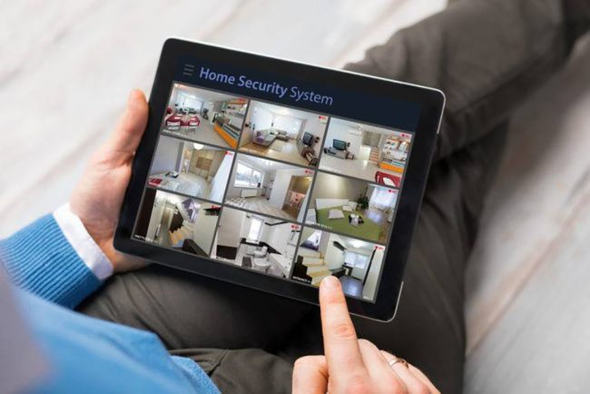 A person holding a tablet displaying a home security app with a grid of live camera
feeds