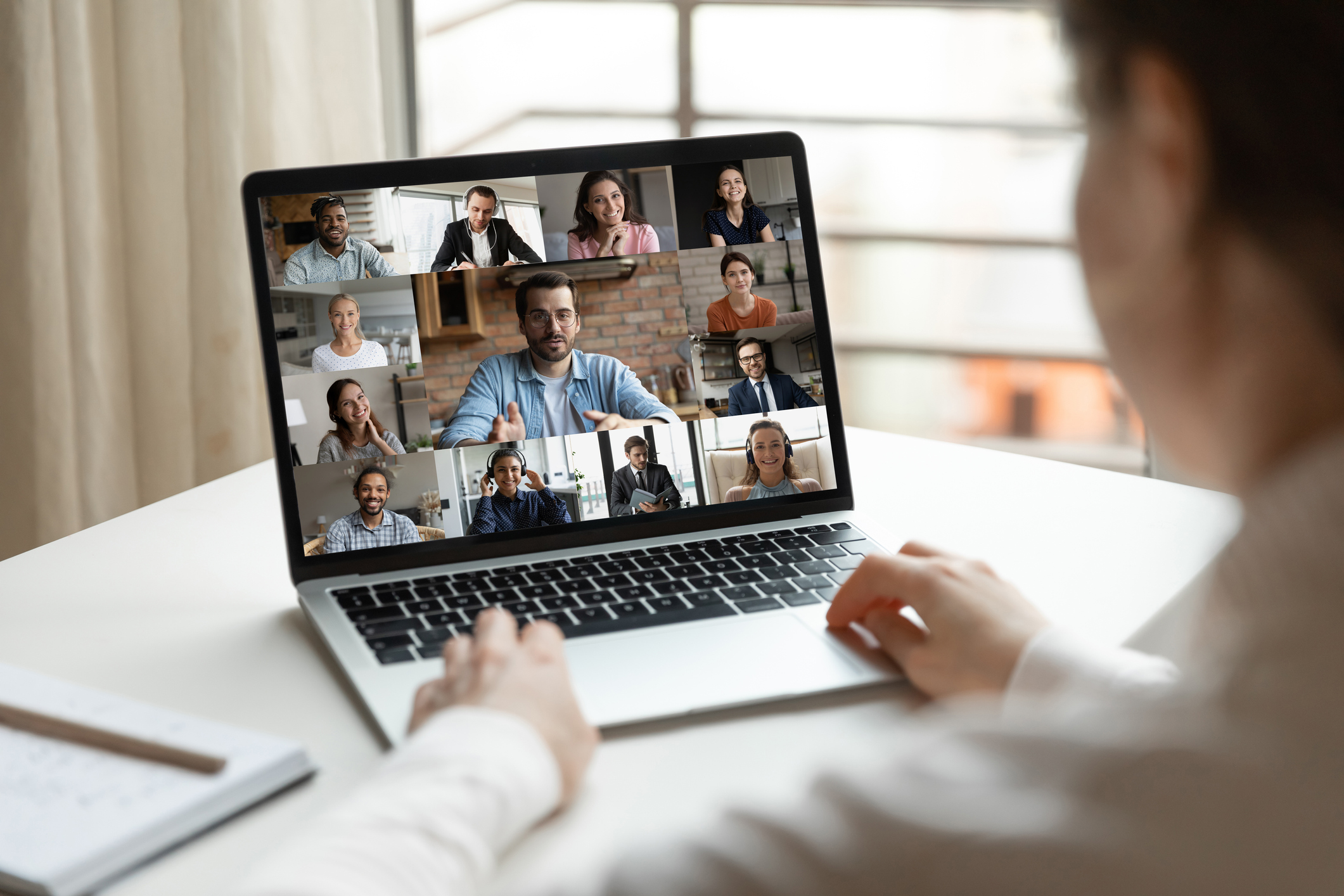 Woman participating in a video call with many other people shown on her laptop screen.