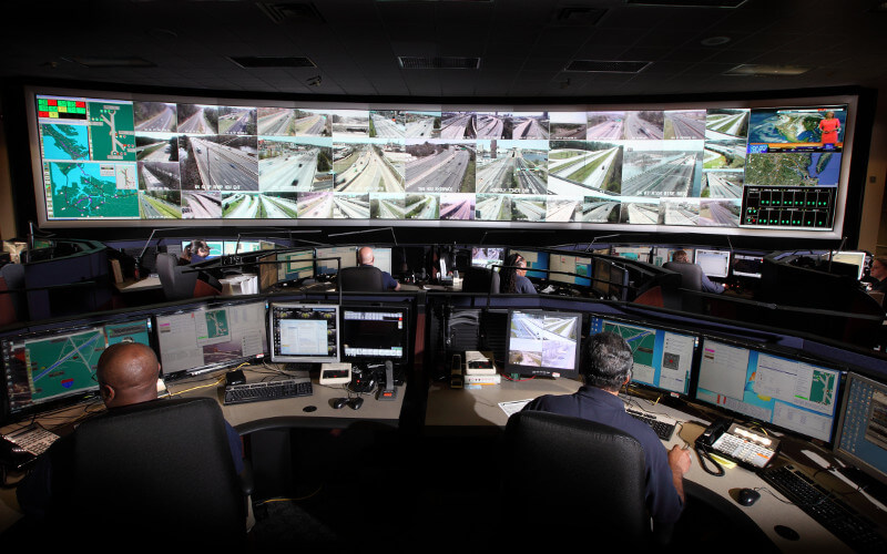 Video surveillance control room with a large wall of monitors showing traffic camera feeds, and operators at workstations.